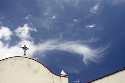 Low angle view of cross and church vane against windy clouds