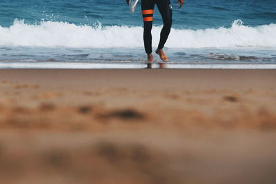 Low section of man with surfboard walking at beach