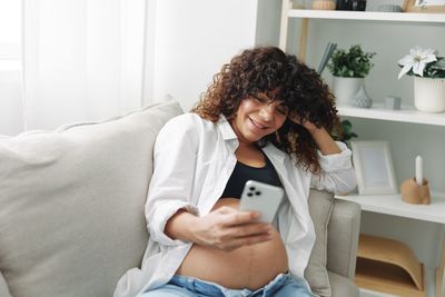 Young woman using mobile phone while sitting on sofa at home