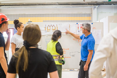 Male instructor teaching trainees while pointing over diagram on whiteboard at workshop