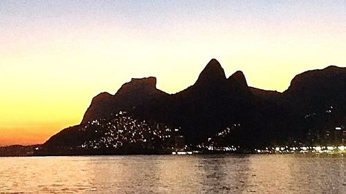 Silhouette mountain by sea against sky during sunset