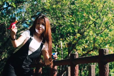 Portrait of smiling woman playing with bubble wand against trees