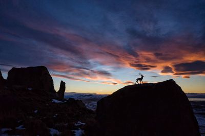 Silhouette man on rock against sky during sunset