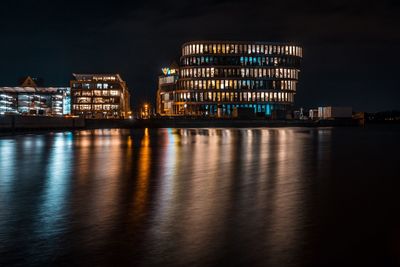 Illuminated city by sea against sky at night