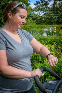 Woman looking at smart watch while holding baby stroller at park