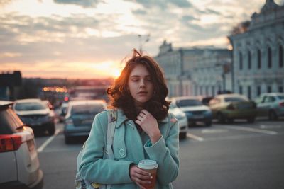 Beautiful young woman in city against sky during sunset