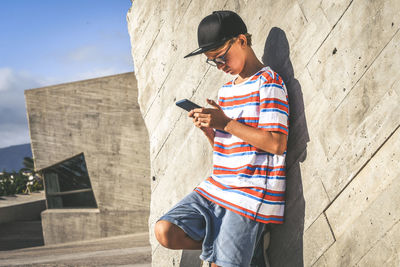 Boy using mobile phone while standing against wall