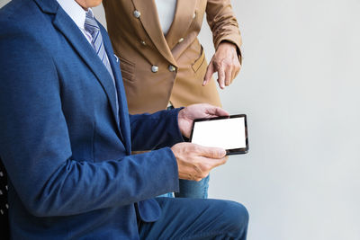 Midsection of businessman with colleague holding digital tablet against wall