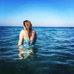 Rear view of woman wearing swimsuit in sea against blue sky