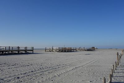 Pier on beach against clear blue sky