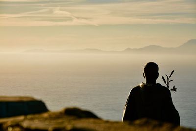 Rear view of silhouette man sitting by sea against sky