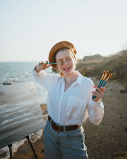 Smiling young woman holding smart phone against sea