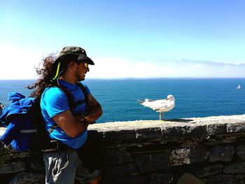Side view of mature man looking at seagull on retaining wall by sea against sky