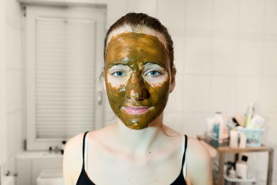 Portrait of young woman with facial mask in bathroom