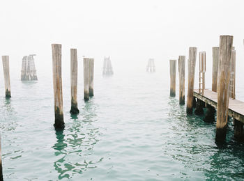 Wooden posts in sea against clear sky