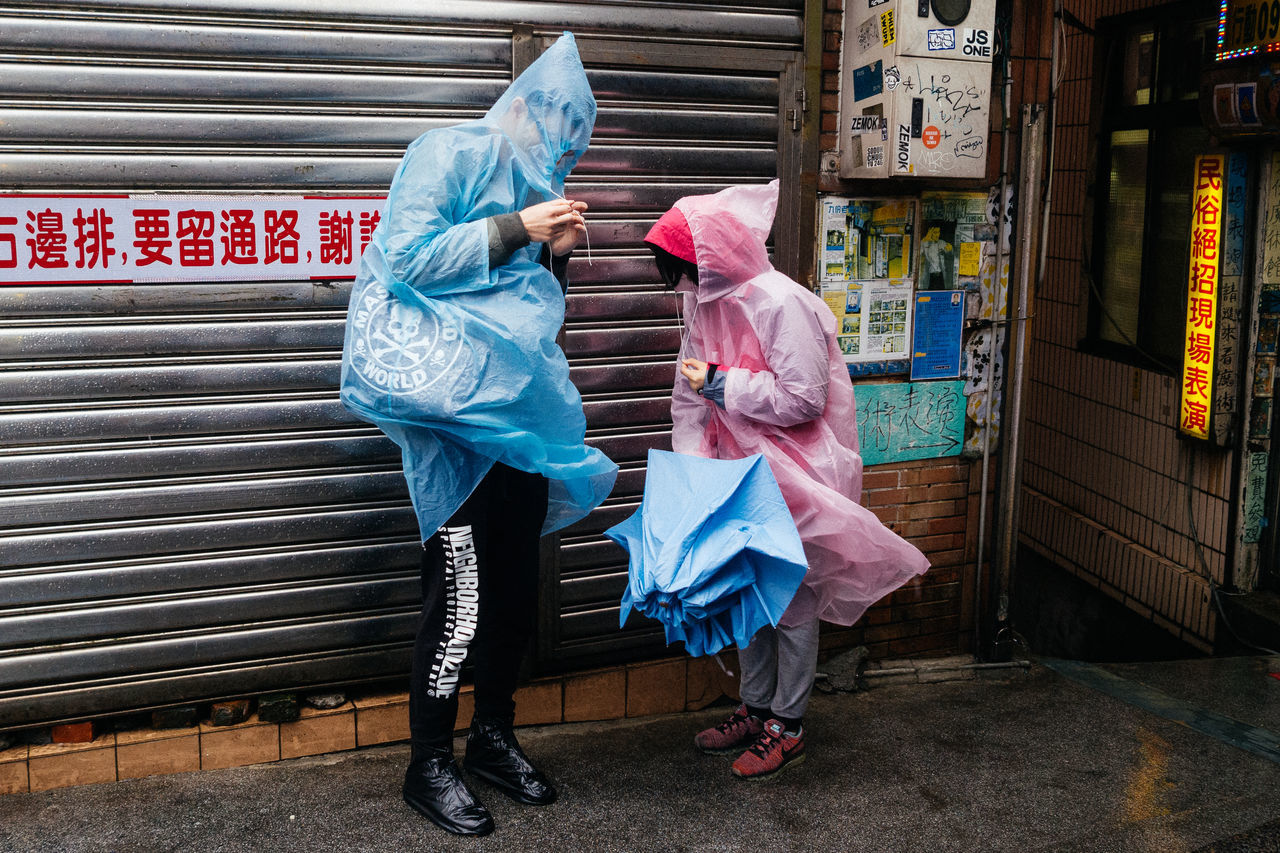 full length, real people, footpath, women, leisure activity, bag, people, day, architecture, city, lifestyles, rear view, clothing, adult, holding, outdoors, protection, building exterior, plastic bag, obscured face