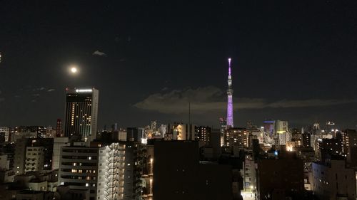 Illuminated modern buildings in city against sky at night