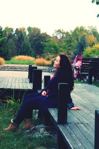 Young woman using mobile phone while sitting against sky