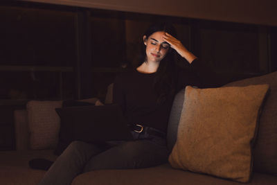 Side view of woman sitting on sofa at home