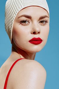 Close-up of young woman wearing hat against blue background