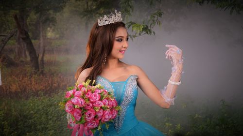 Beautiful woman in blue dress holding bouquet while standing on field at park
