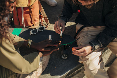 Midsection of man painting fingernails of female friend sitting near skateboard