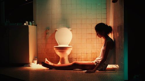 Side view of woman sitting in bathroom