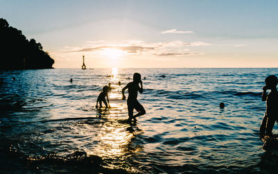 Silhouette people enjoying in sea against sky during sunset