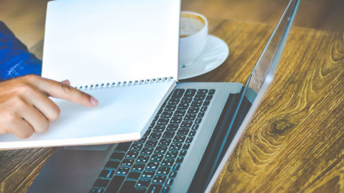 Close-up of businessman holding book with laptop on table