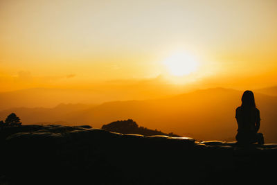 Silhouette person on rock against sky during sunset