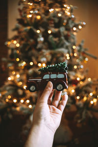 Cropped hand of woman holding toy car against illuminated christmas tree