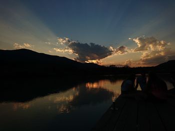 Scenic view of lake by silhouette mountain against sky during sunset