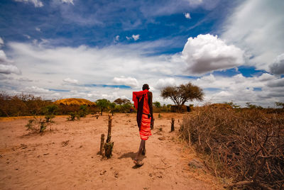 Rear view of man standing on field against sky masai village