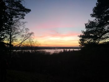 Silhouette trees by lake against sky during sunset