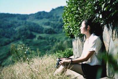 Side view of woman sitting on by wall on mountain