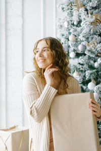 Happy girl holding a gift box wrapped in craft paper and sitting near the christmas tree