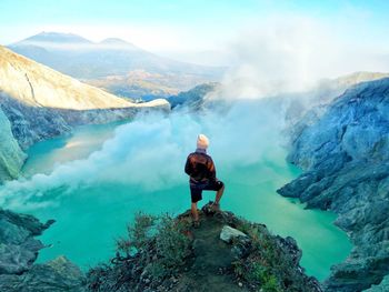 Rear view of man standing on rocks against mountains