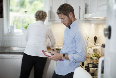 Man using digital tablet with mother cooking in kitchen