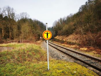 Road sign by railroad tracks against sky