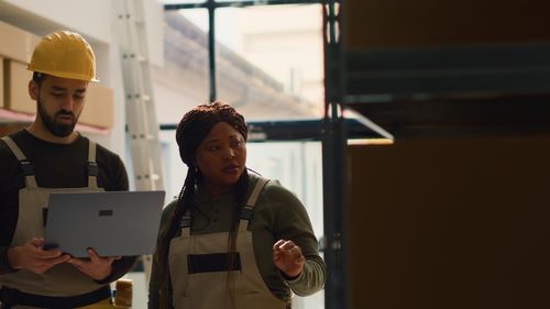 Portrait of young woman using mobile phone while standing in factory