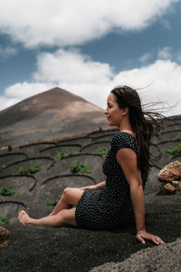 Beautiful young woman sitting on land against sky