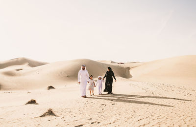 People walking on sand dune in desert against clear sky