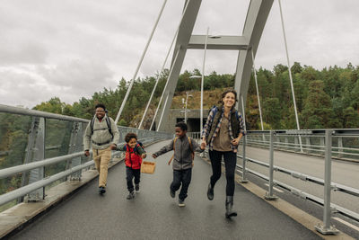 Happy family holding hands while running on bridge during vacation