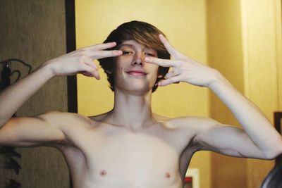 Close-up portrait of shirtless young man showing hand sign at home