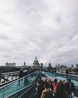 People at london millennium footbridge with st paul cathedral against cloudy sky