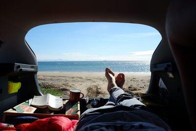 Low section of person relaxing in car against sea