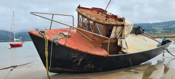 Abandoned boat moored on beach against sky