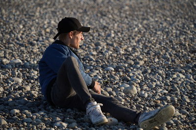 Side view of young man sitting at beach