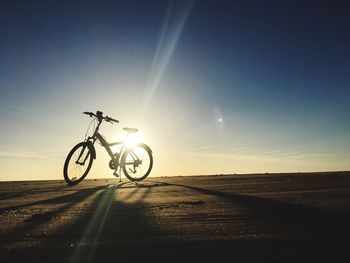 Bicycle on beach against sky during sunset