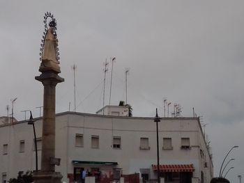 Low angle view of communications tower amidst buildings against sky